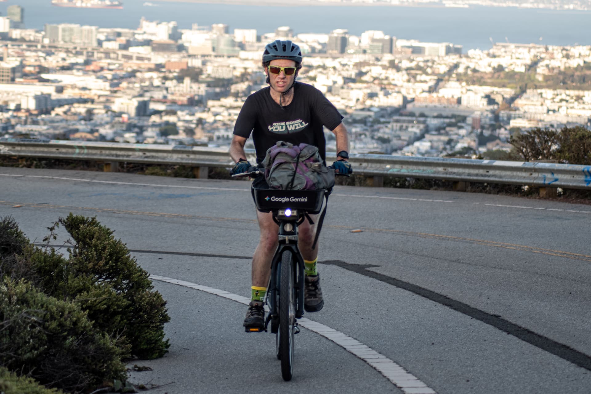 Grinding uphill on a Lyft bike toward the top of Twin Peaks, bay and skyline in the background