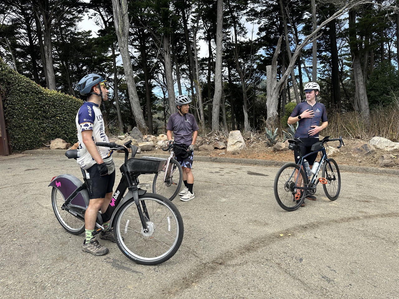 Three riders chatting in a clearing, one standing next to a Lyft bikeshare bike between two road bikes